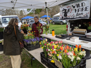 Farmer Leah Cook of Wild Hare Farm demonstrates what she calls the market's new "purchasing in a pandemic" policy as she has customers point to what they want so that she can pull the order together.