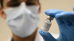 A masked doctor holds a vial of the COVID-19 vaccine in his gloved hand. Photo by Lisa Ferdinando and sourced from Wikipedia Commons.