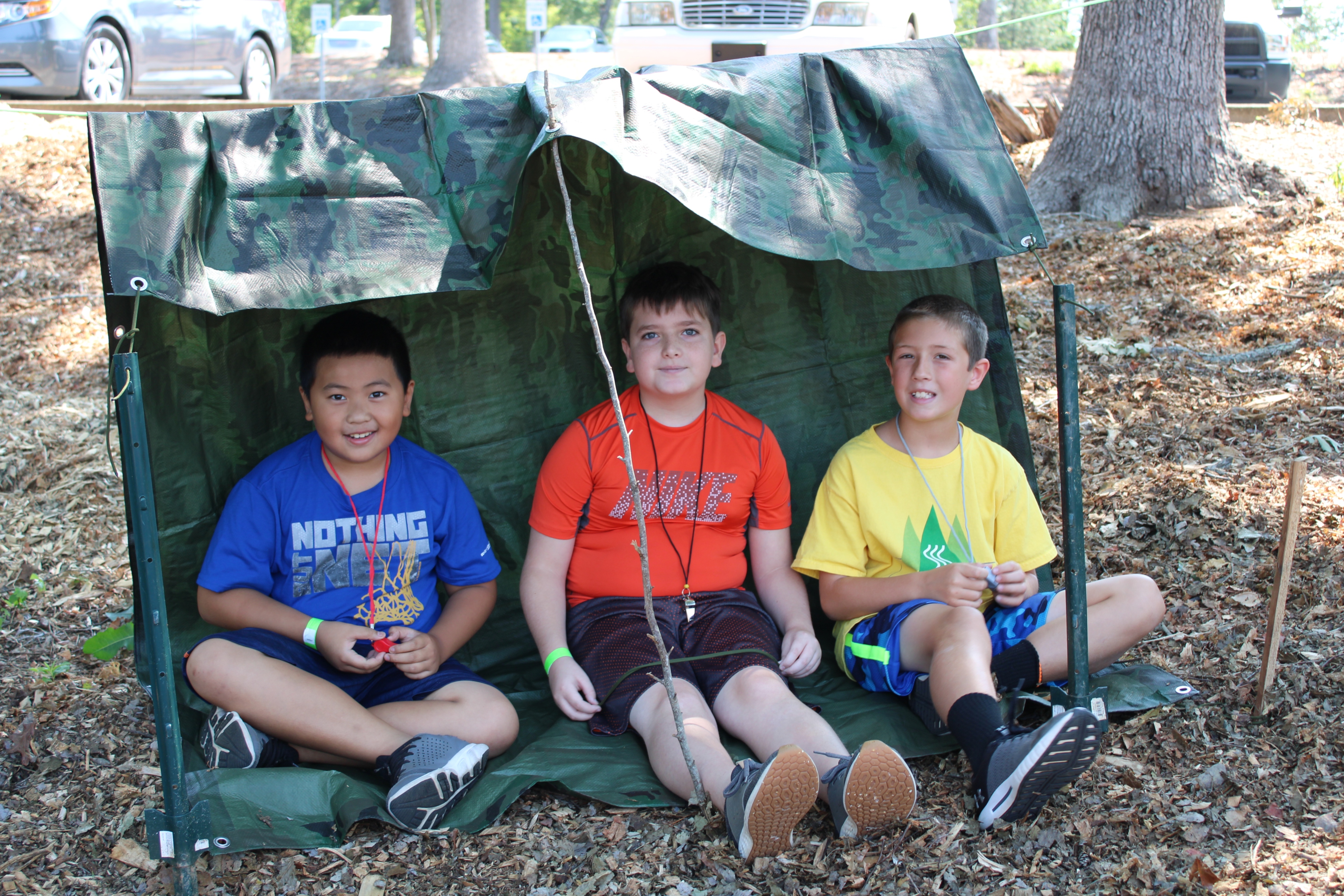 From the 4-H archives, three Caldwell County youth pose during Summer Exploring under their structure after a shelter-building activity. Hands-on practice helps youth learn emergency preparedness skills.