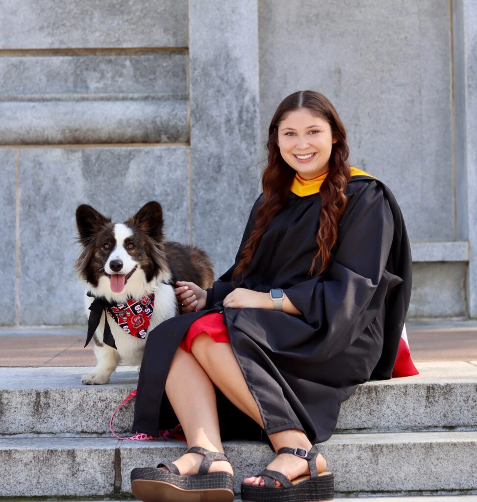 A girl in graduation gown poses with dog.