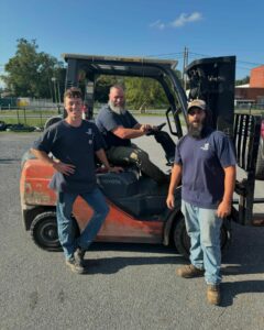 1 man sitting in forklift and 2 men standing around forklift