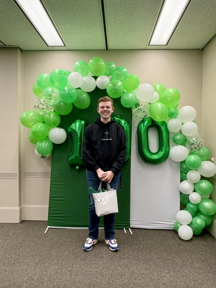 Peyton Denning stands in front of green and white balloons