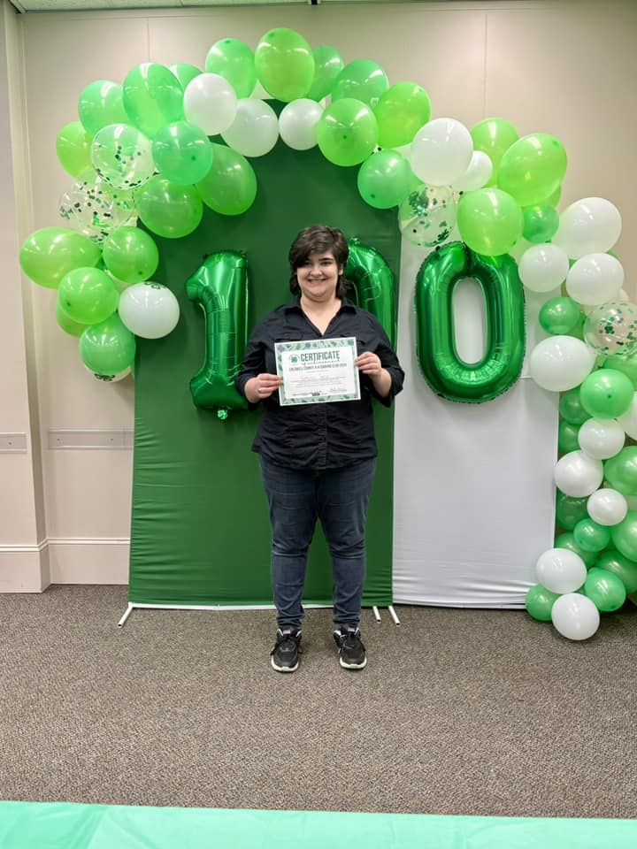 Katherine Taylor stands in front of green and white balloons