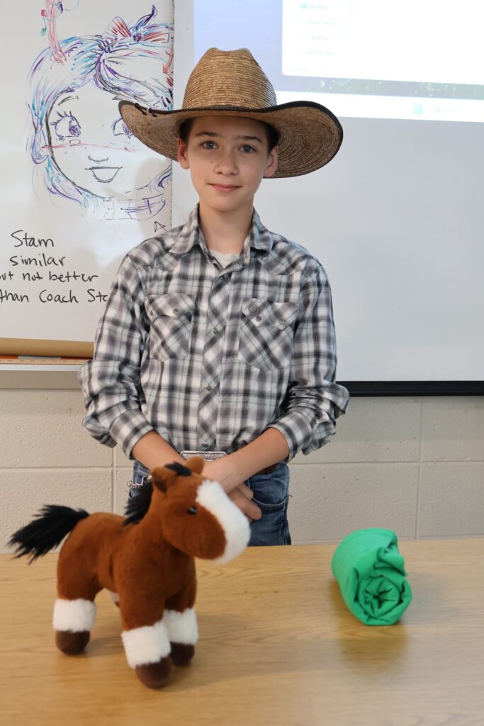 boy in cowboy hat standing at a table with stuffed horse in the foreground